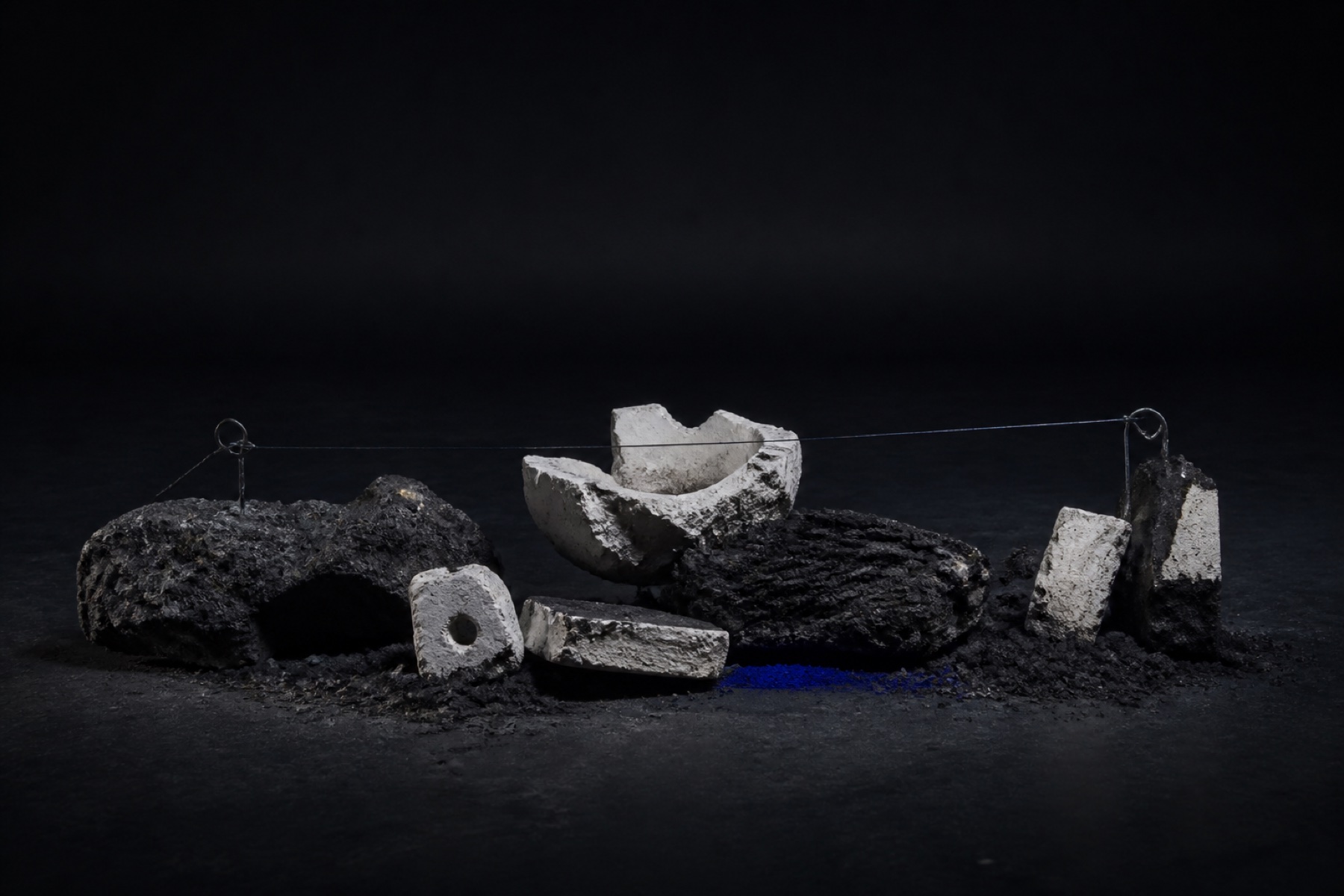Original concept study of dark mineral fragments connected by a taut wire